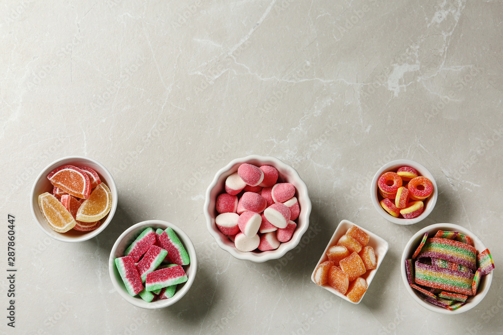 Flat lay composition with bowls of different jelly candies on light marble background. Space for text Flat lay composition with bowls of different jelly candies on light marble background. Space for text