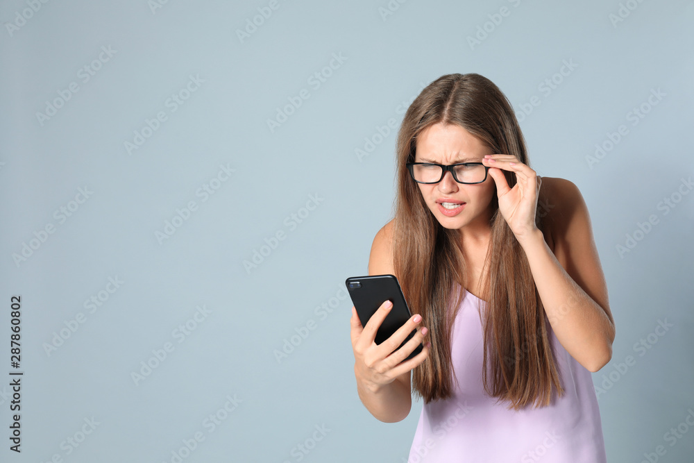 Young woman with vision problems using smartphone on grey background, space for text Young woman with vision problems using smartphone on grey background, space for text