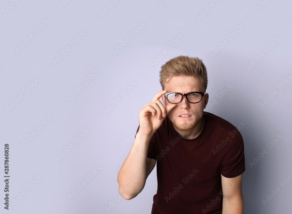 Young man with vision problem wearing glasses on light background Young man with vision problem wearing glasses on light background