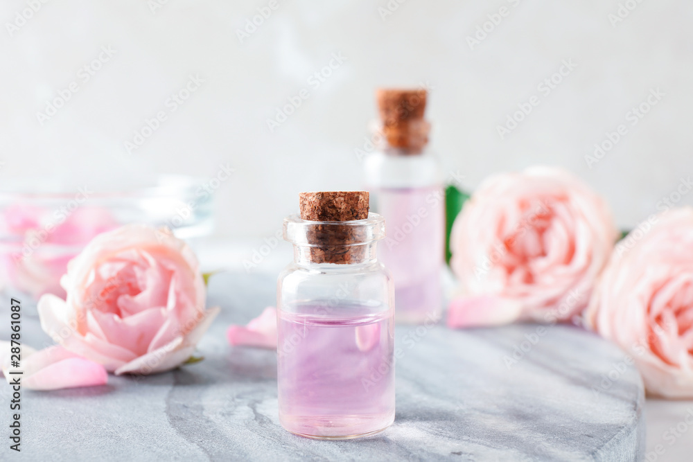 Bottles with rose essential oil and flowers on stone board Bottles with rose essential oil and flowers on stone board