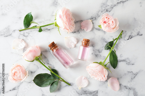 Flat lay composition with rose essential oil and flowers on marble table