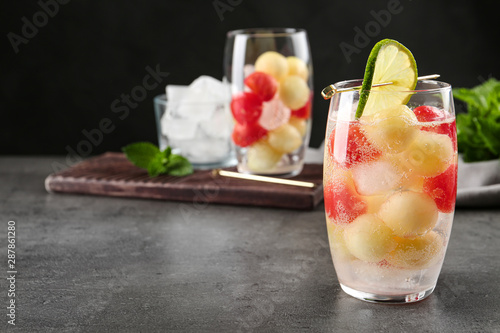 Glass of melon and watermelon ball cocktail with lime on grey table. Space for text