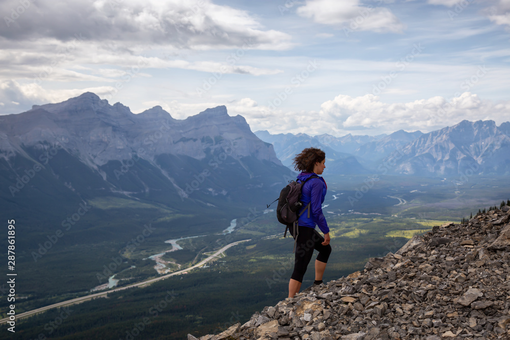 Adventurous Girl is hiking up a rocky mountain during a cloudy and rainy day. Taken from Mt Lady MacDonald, Canmore, Alberta, Canada.