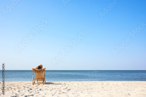 Young woman relaxing in deck chair on sandy beach
