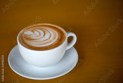 A white cup of cappuccino with latte art on brown wood table with low light.
