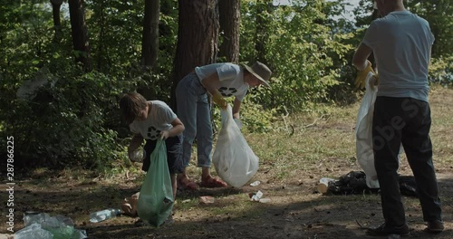 Team of positive volunteers collecting trash in contamined green wood landscape on sunny day. Ecology problems. Overconsumption concept. photo