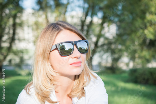 Close up image of happy blonde woman in sunglasses and autumn clothes posing sideways outdoors