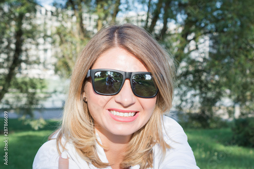 Close up image of happy blonde woman in sunglasses and autumn clothes posing sideways outdoors