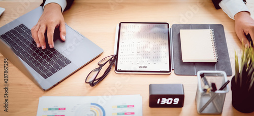 Businessman planner a schedule in the calendar on digital tablet and hands press laptop computer at office.