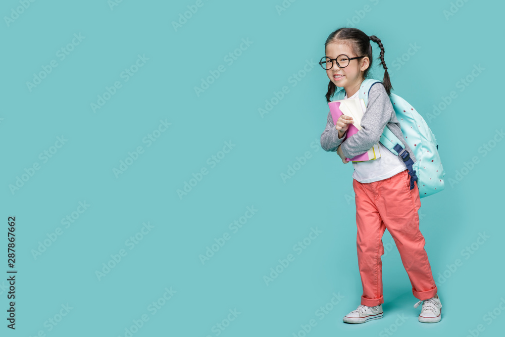Beautiful smiling Asian little girl with glasses and hold a books with school bag is back to school, empty space in studio shot isolated on colorful blue background, Educational concept for school - obrazy, fototapety, plakaty 