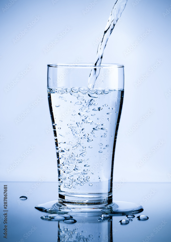 Pouring fresh pure water from bottle into a glass on the table with water drops, Healthcare and beauty hydration concept Pouring fresh pure water from bottle into a glass on the table with water drops, Healthcare and beauty hydration concept