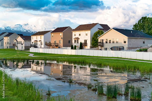 Homes and cloudy sky reflected on the shiny surface of a grassy pond