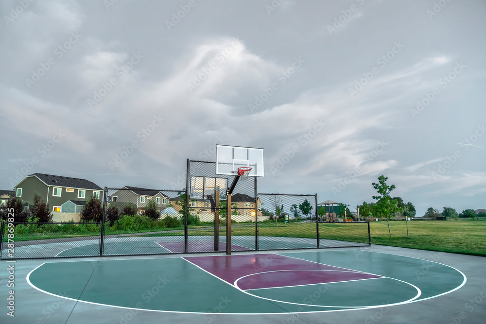 Basketball courts at a park near multi storey family homes under cloudy sky