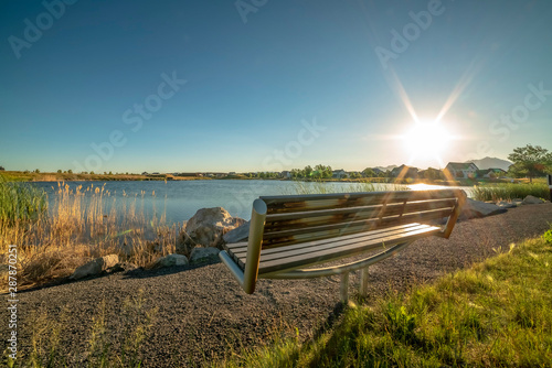 Empty bench with a view of scenic lake bright sun and cloudless blue sky