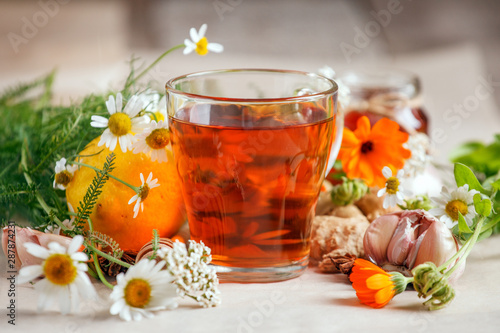 Cup of herbal tea and fresh flowers, lemin, garlic, ginger root on wooden background - seasonal immunity treatment, remedy, cold flu alternative medicine