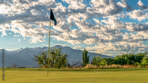 Panorama Focus on the flagstick of a golf course against trees mountain and cloudy sky