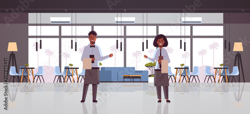 professional waiters couple holding menu warmly welcoming to cozy restaurant man woman workers in apron showing hospitality modern cafe interior flat full length horizontal