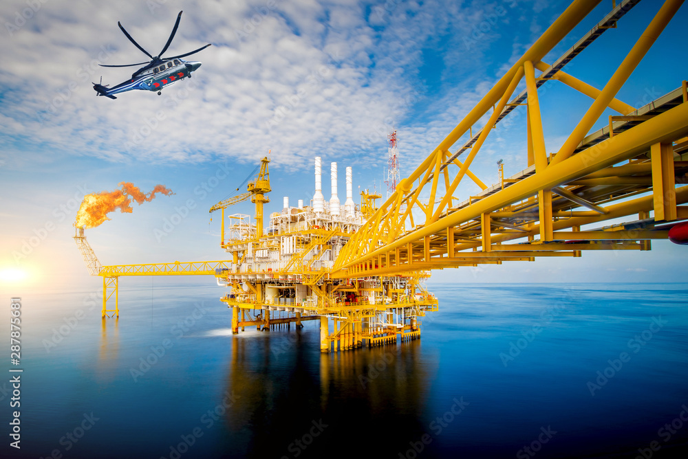 Offshore oil and gas rig platform with offshore helicopter transporting to oil rig at beautiful sky in the gulf of Thailand.