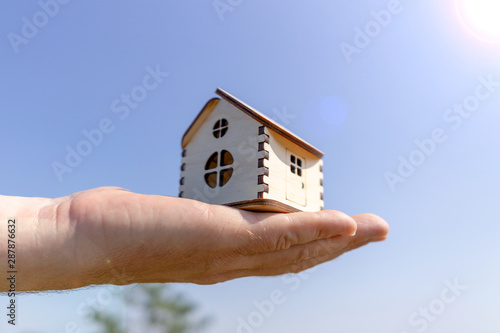 Man holds out a small wooden house in the palm of his hand. Close-up