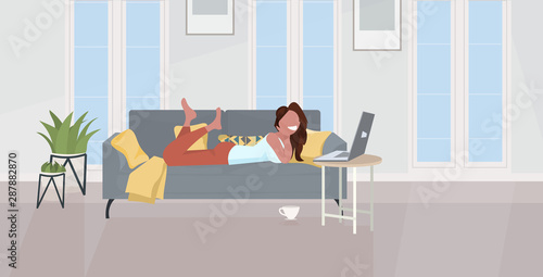 girl lying on sofa using laptop happy woman relaxing at home modern living room interior horizontal full length flat