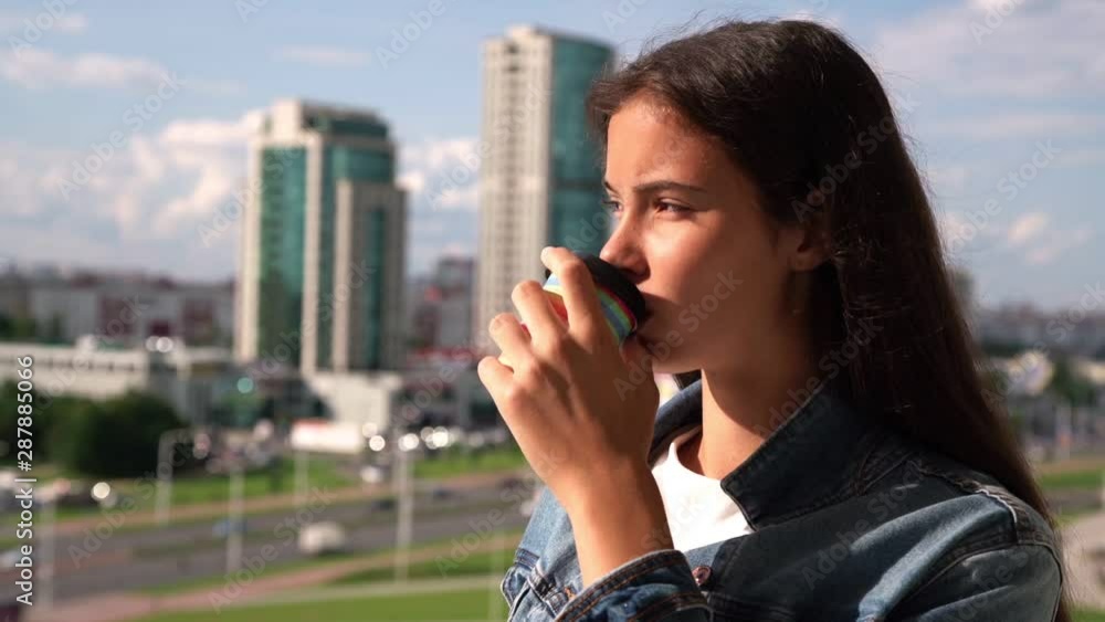 attractive girl teenager with loose hair drinks coffee and admires pictorial cityscape on sunny day slow motion closeup attractive girl teenager with loose hair drinks coffee and admires pictorial cityscape on sunny day slow motion closeup