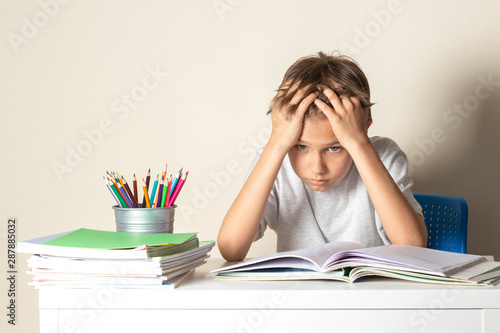 Tired upset schoolboy with pile of school books and notebooks photo