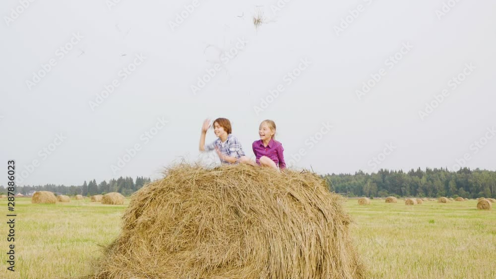 Happy teenagers throwing up dry straw on haystack. Carefree boy and girl teenagers jumping on haystack at harvesting field. Friends having fun on countryside field Happy teenagers throwing up dry straw on haystack. Carefree boy and girl teenagers jumping on haystack at harvesting field. Friends having fun on countryside field