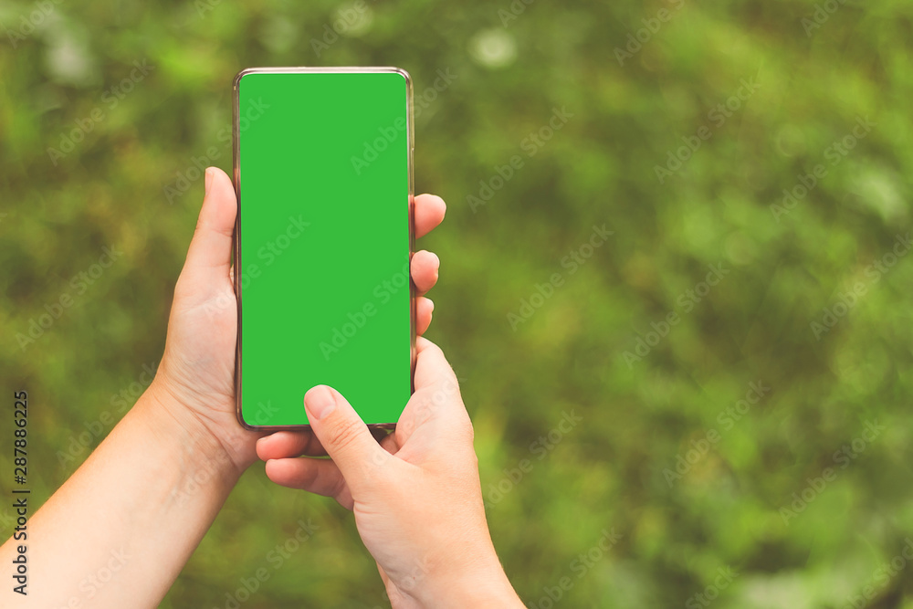 Woman's hand holding the phone with isolated green screen. Copy space. Blurred background.