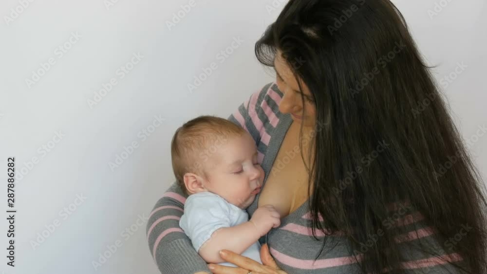 Young beautiful mother with long dark hair is holding a newborn infant baby of two months on a white background in studio Young beautiful mother with long dark hair is holding a newborn infant baby of two months on a white background in studio