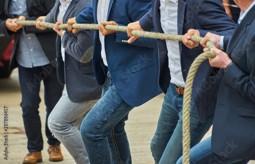 Men with business clothing and formal jackets pulling together on a thick rope, concept photo of the expression "pulling together".