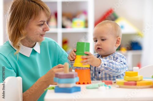 Baby with mother in nursery at home. Child with teacher playing with educational cup toys in daycare or creche
