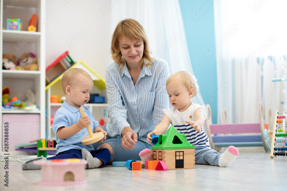 Children with teacher playing with educational toys in kindergarten. Babies with carer in creche or nursery school Children with teacher playing with educational toys in kindergarten. Babies with carer in creche or nursery school