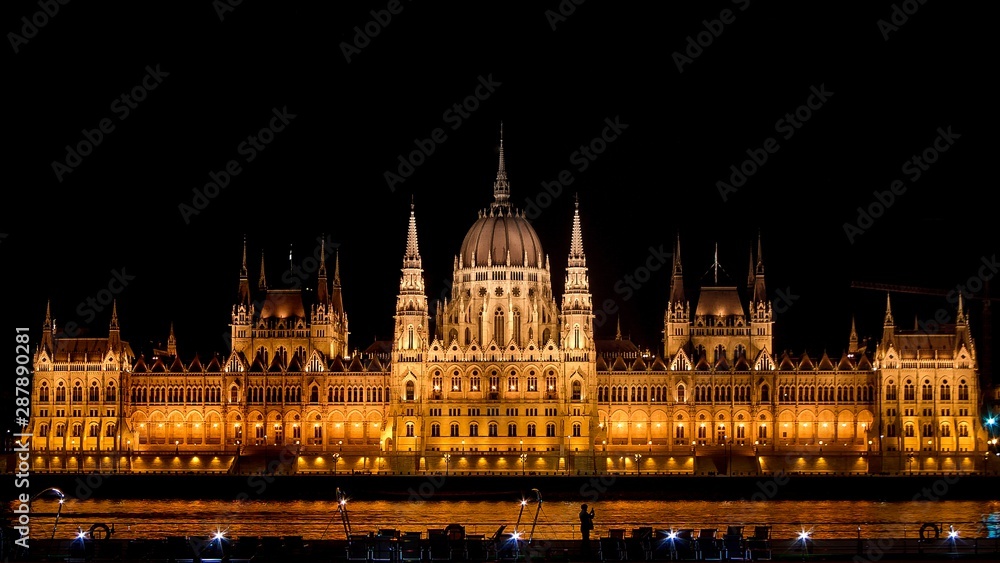 Panoramic background orange  night image of Budapest parlament from the  front with boat and tourist taking a photo of the city.