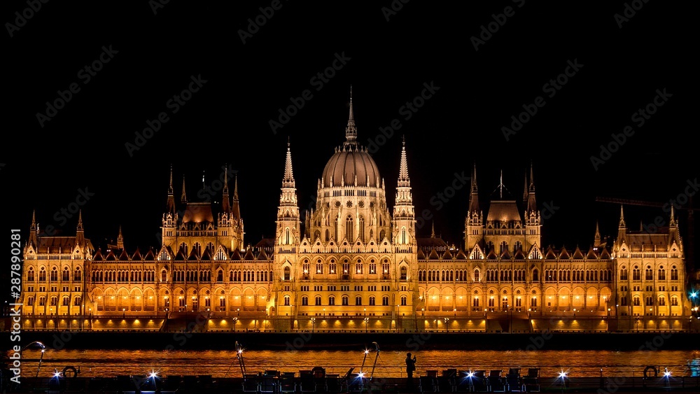 Panoramic background orange night image of Budapest parlament from the front with boat and tourist taking a photo of the city. Panoramic background orange night image of Budapest parlament from the front with boat and tourist taking a photo of the city.