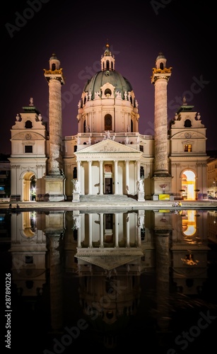 Karlskirche basilica at night and pond with reflectiosn and tourists sittng around. Artistic purple vibe background image in Viena.
