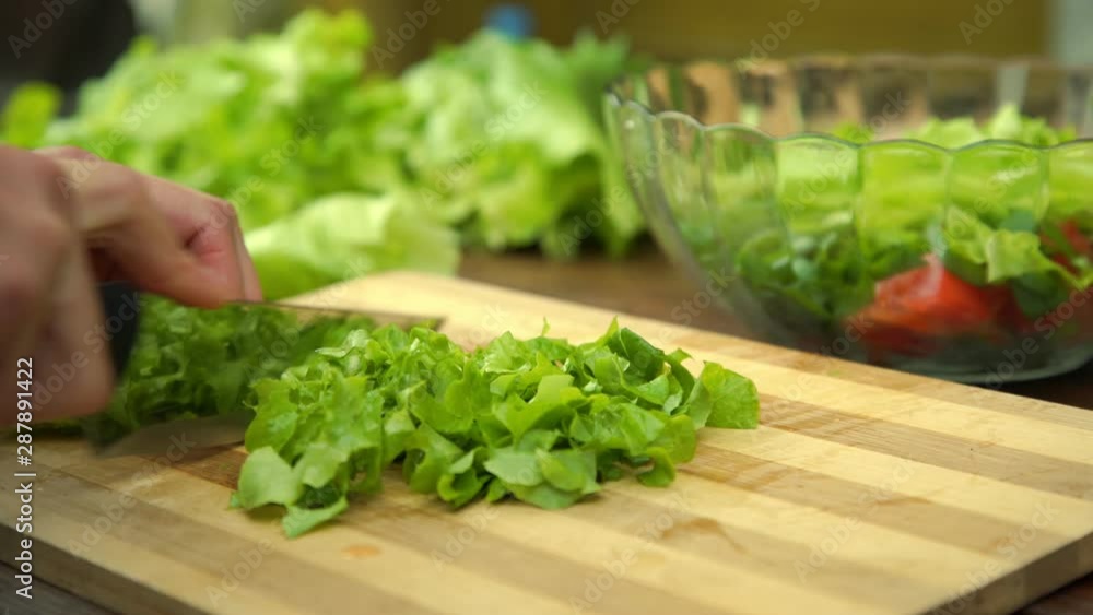 woman hands hold big silver knife and cut fresh green lettuce leaves on wooden kitchen board extreme close view woman hands hold big silver knife and cut fresh green lettuce leaves on wooden kitchen board extreme close view