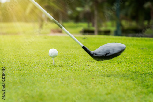 Close up golf club and golf ball ,professional golfer teeing golf ball to hole at golf course to win in game ,green grass and sunlight rays background. 