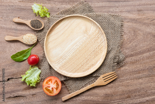 Empty wooden plate and frame of spices, herbs and vegetables on sack fabric background