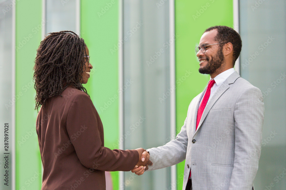 Business partners greeting each other near office. Business man and woman standing outside and shaking hands with each other. Partnership concept Business partners greeting each other near office. Business man and woman standing outside and shaking hands with each other. Partnership concept