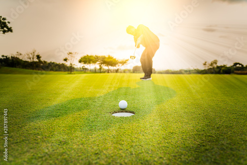 Silhouette golfer professional teeing golf ball to hole to winner in game at golf course with sunlight rays 
