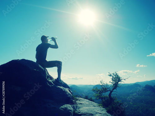 Traveler on rock drinking bottled water from plastic bottle