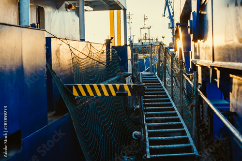 Stern of cargo vessel at port. Gangway arrangment. Blue hull.