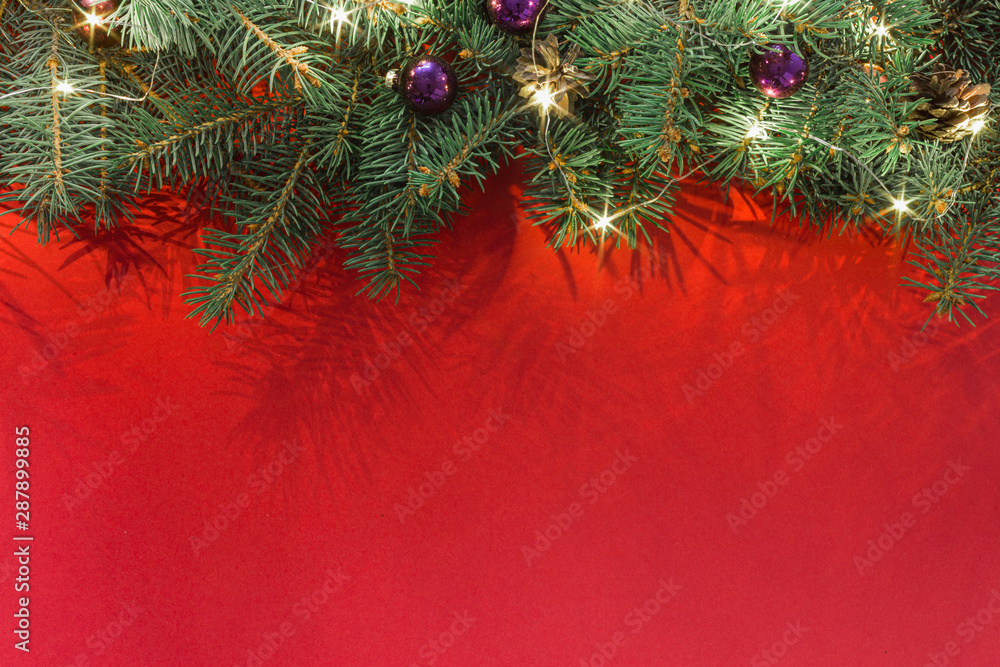 Spruce branches with christmas balls and garland on a red background top view Spruce branches with christmas balls and garland on a red background top view