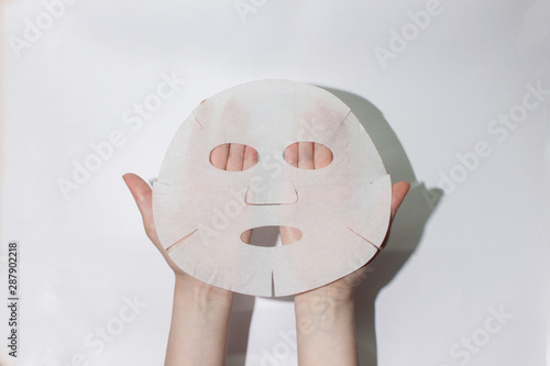  Sheet face mask. Fabric mask for facial skin. Female hands hold a face mask. On a white background. View from above. Cosmetology, medicine and healthcare. The concept of home treatments for moisturiz photo