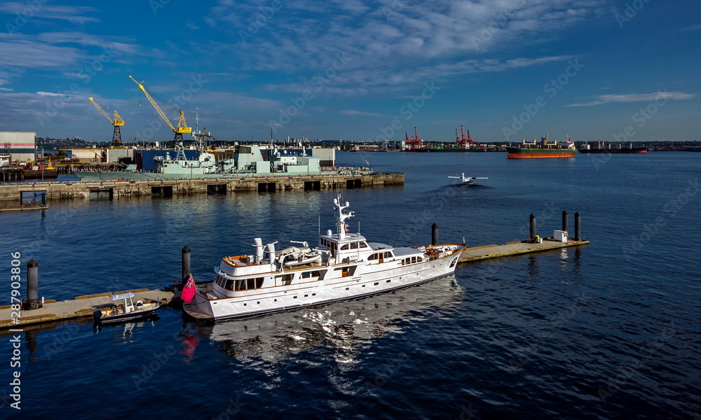 Vancouver Harbor commercial cargo port and marina for pleasure yachts, warship moored at the pier, hydroplane on take-off, Vancouver City on the horizon on the background of blue cloudy sky Vancouver Harbor commercial cargo port and marina for pleasure yachts, warship moored at the pier, hydroplane on take-off, Vancouver City on the horizon on the background of blue cloudy sky