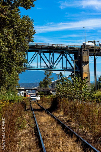Railroad under a bridge in an industrial area with forestation, rail-car on rails