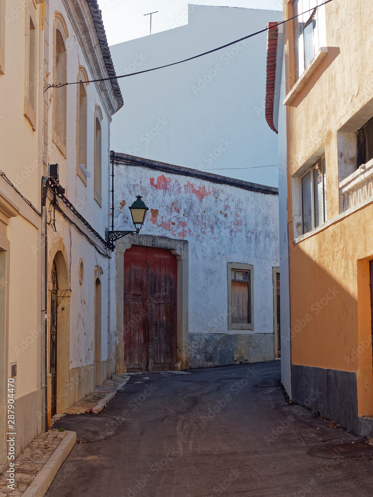 A narrow side street during Siesta in the small Portuguese town of Estoi in the Algarve, with an ornate street lamp attached to the walls of the houses. Portugal.