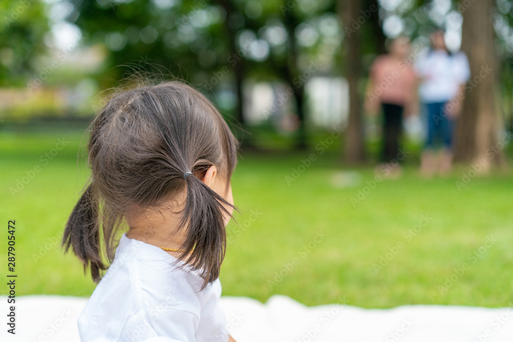 young girl looks back to her parent standing farway while she's plaing on the white mat in the garden. young girl looks back to her parent standing farway while she's plaing on the white mat in the garden.
