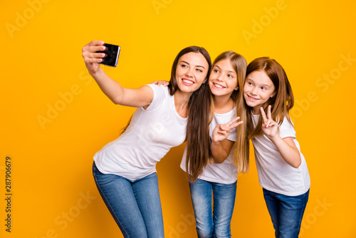 Photo of three ladies holding telephone taking selfies with v-sign symbols wear casual clothes isolated yellow background