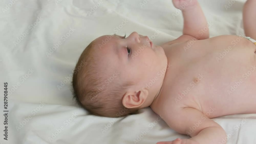 Portrait of beautiful funny little newborn baby of two months lying on white bed. Mom dresses the baby Portrait of beautiful funny little newborn baby of two months lying on white bed. Mom dresses the baby